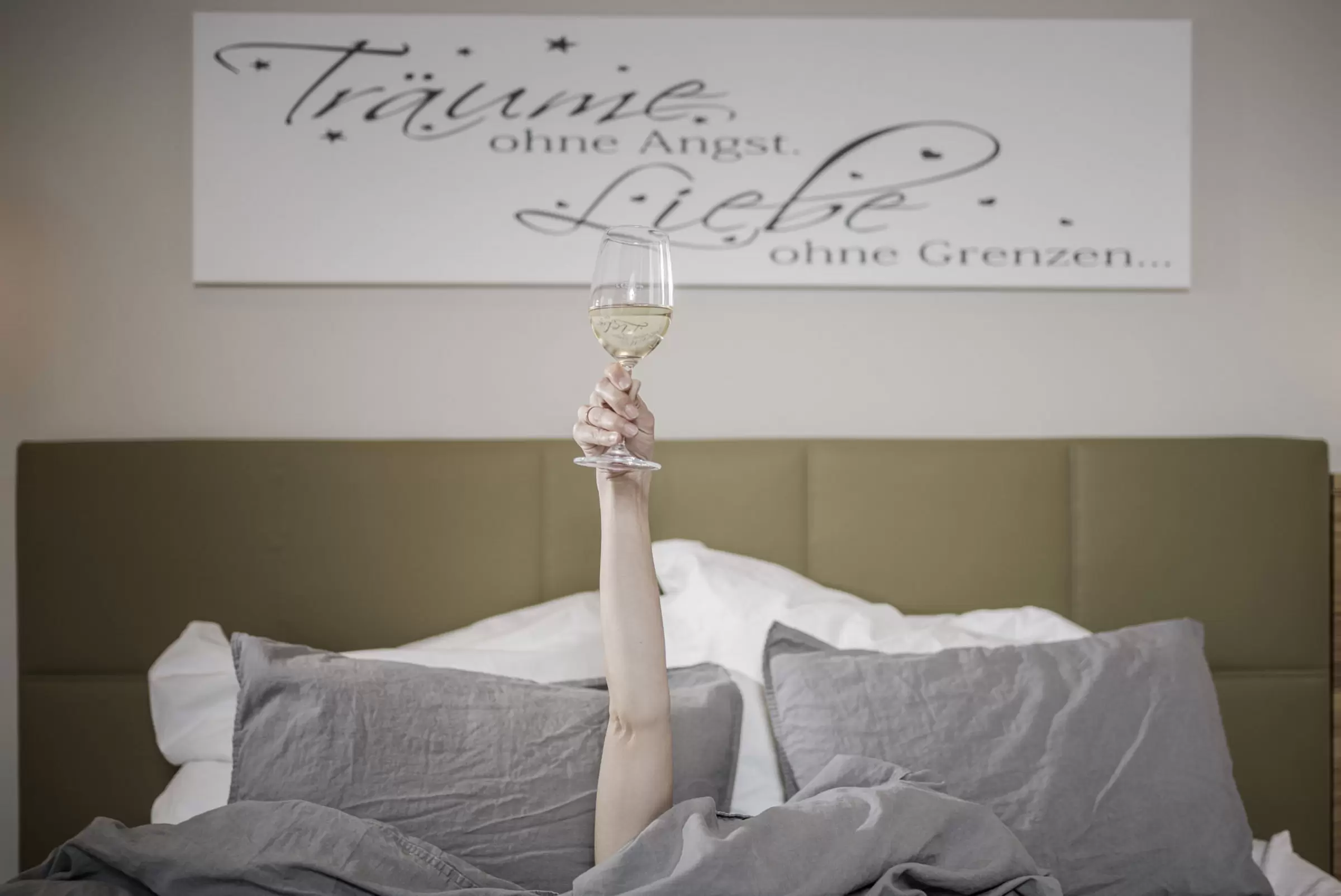 Jordans Untermühle - Wohlfühlzimmer - Arm mit vollen Weinglas aus dem Bett herausgestreckt